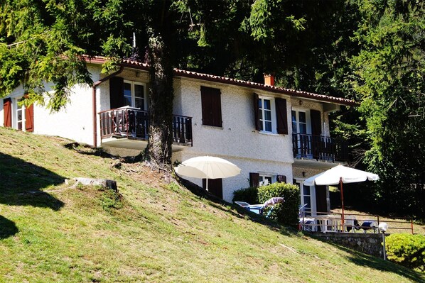 A two-story house with a balcony, a covered patio with umbrellas, and a stone wall.