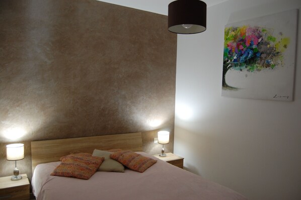 A bedroom with a bed, two bedside lamps, a nightstand, and a wall painting.