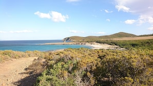 A coastal landscape with a rocky beach, dense shrubbery, and a distant hill. - LARGE VILLA - 4 **** - HEATED SWIMMING POOL, 180° SEA VIEW - AIR CONDITIONED 
 (Sisco)
