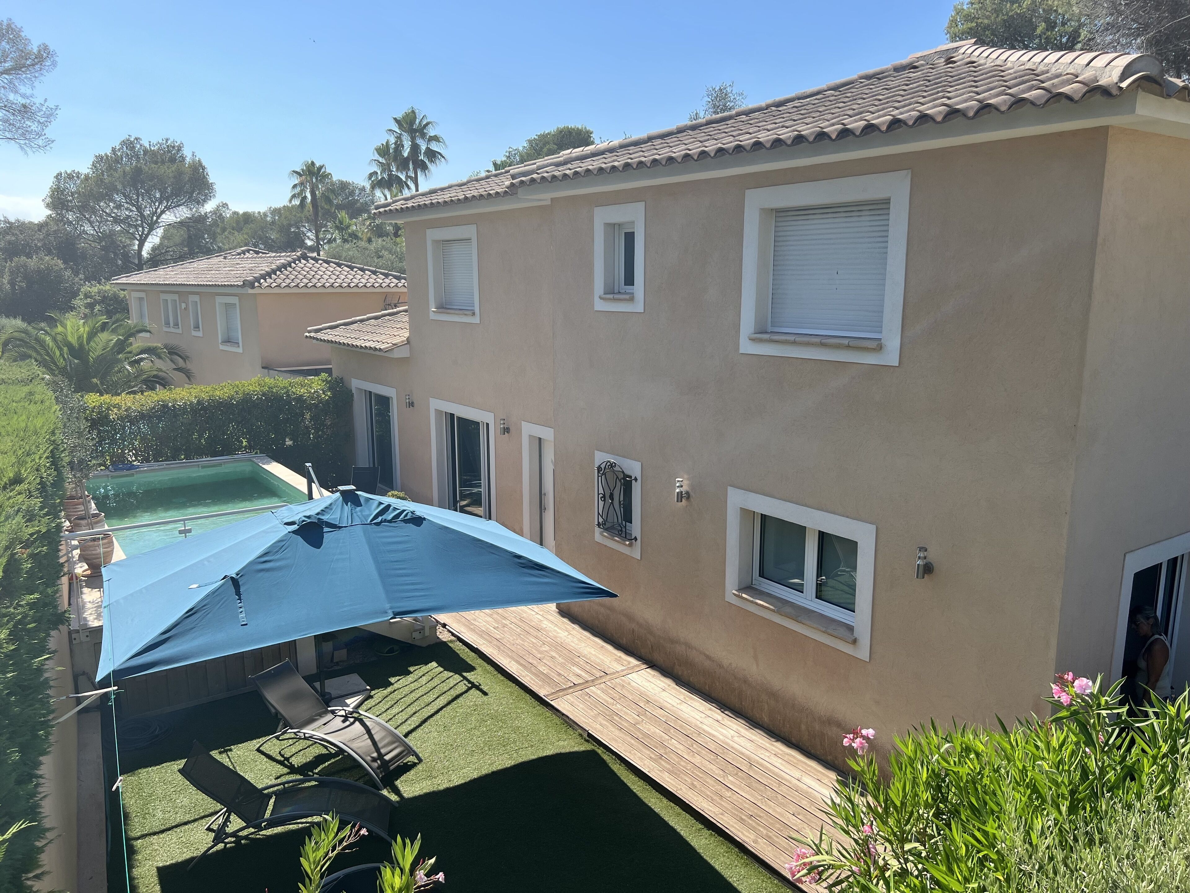 A two-story house with a swimming pool, a covered patio with outdoor furniture, and a well-maintained garden.