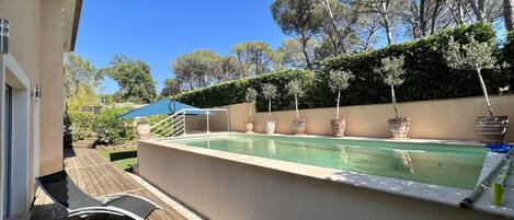 A swimming pool with a wooden deck, lounge chairs, and potted plants.