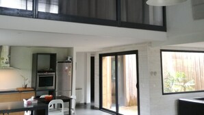 A modern kitchen with a dining area, large windows, and a high ceiling.