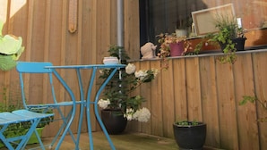 A wooden exterior wall with a window, a blue metal table, and potted plants.