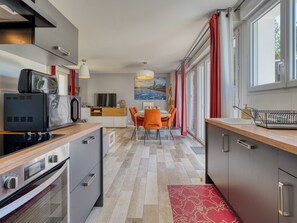 A modern kitchen with a microwave, stove, and dining area with chairs and a table. - Villa Russie - Domaine Le Sherwood (Notre-Dame-De-Monts)