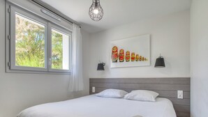 A bedroom with a large bed, a window with curtains, a wall-mounted artwork, bedside lamps, and a bedside table.