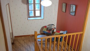 Una escalera con baranda de madera, un ventanal con vista al exterior y una pared con papel tapiz estampado.