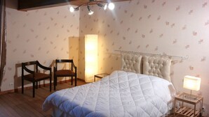 Un dormitorio con una cama grande, dos sillas de madera, una mesita de noche con una lámpara y una cortina.