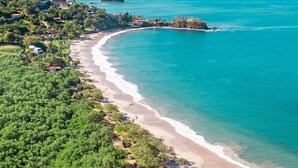Eine Luftaufnahme einer Küstenlandschaft mit Sandstrand, üppiger Vegetation und blauem Meer.