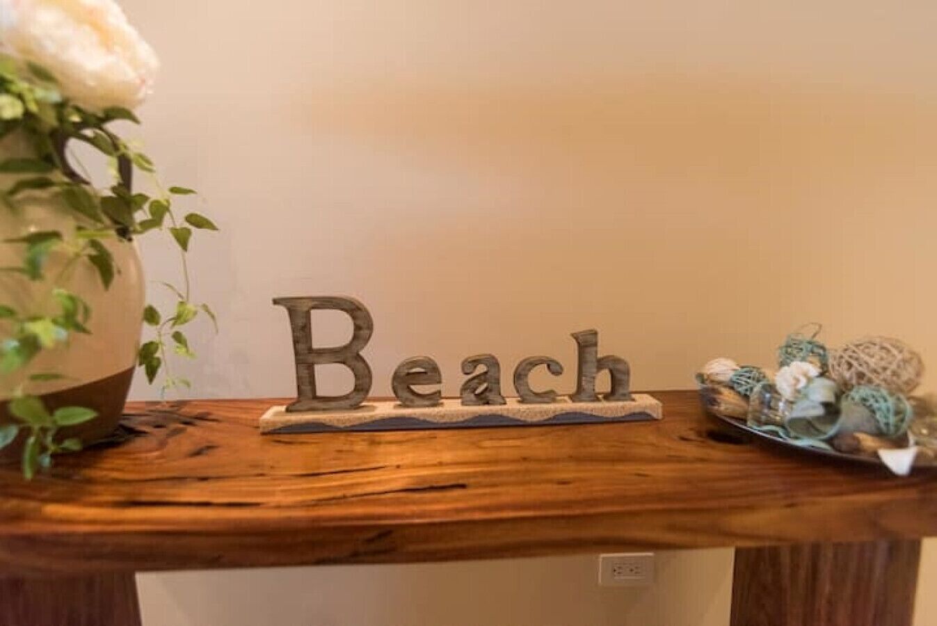 Ett träbord med en skylt med texten ”Beach”, en krukväxt och dekorativa föremål.