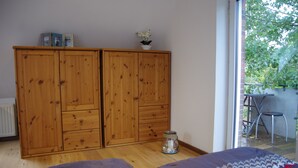 A bedroom with a wooden wardrobe, a small table with a chair outside the window, and a bed with patterned bedding. - Apartment "Cockle" for 2P, at the North Sea between Dornumersiel and Bensersiel (Dornum)