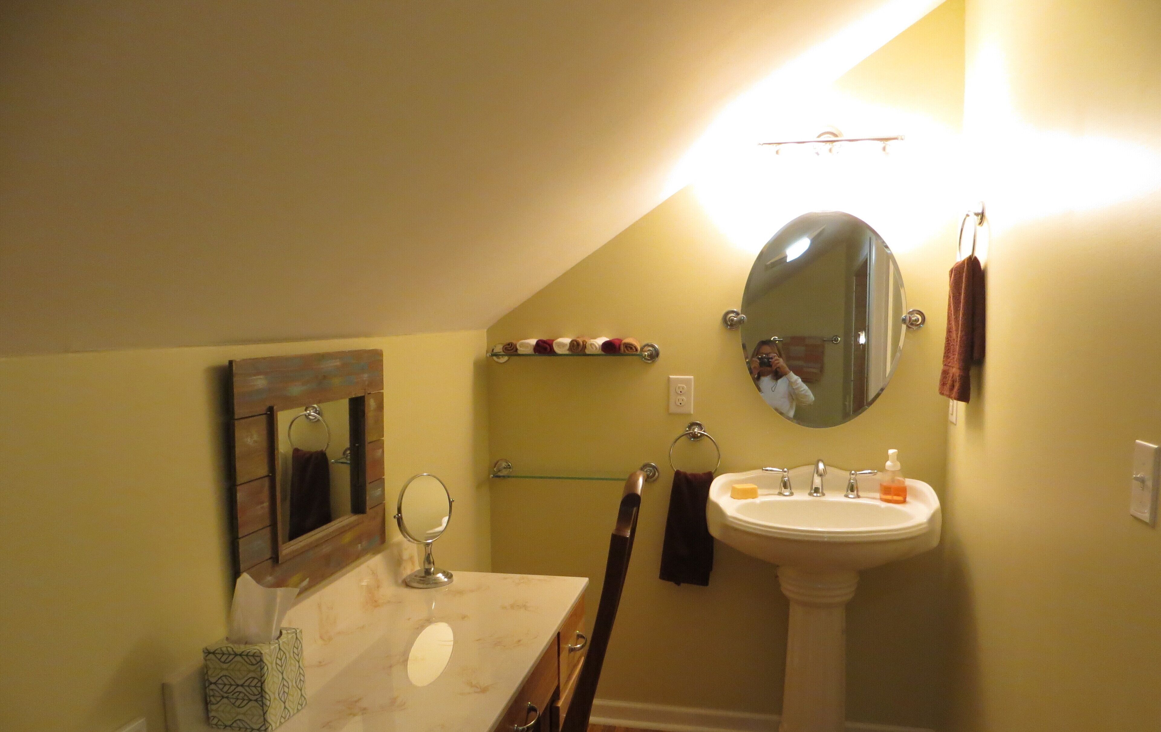 A bathroom with a vanity, sink, mirror, towel rack, and a shelf with toiletries.