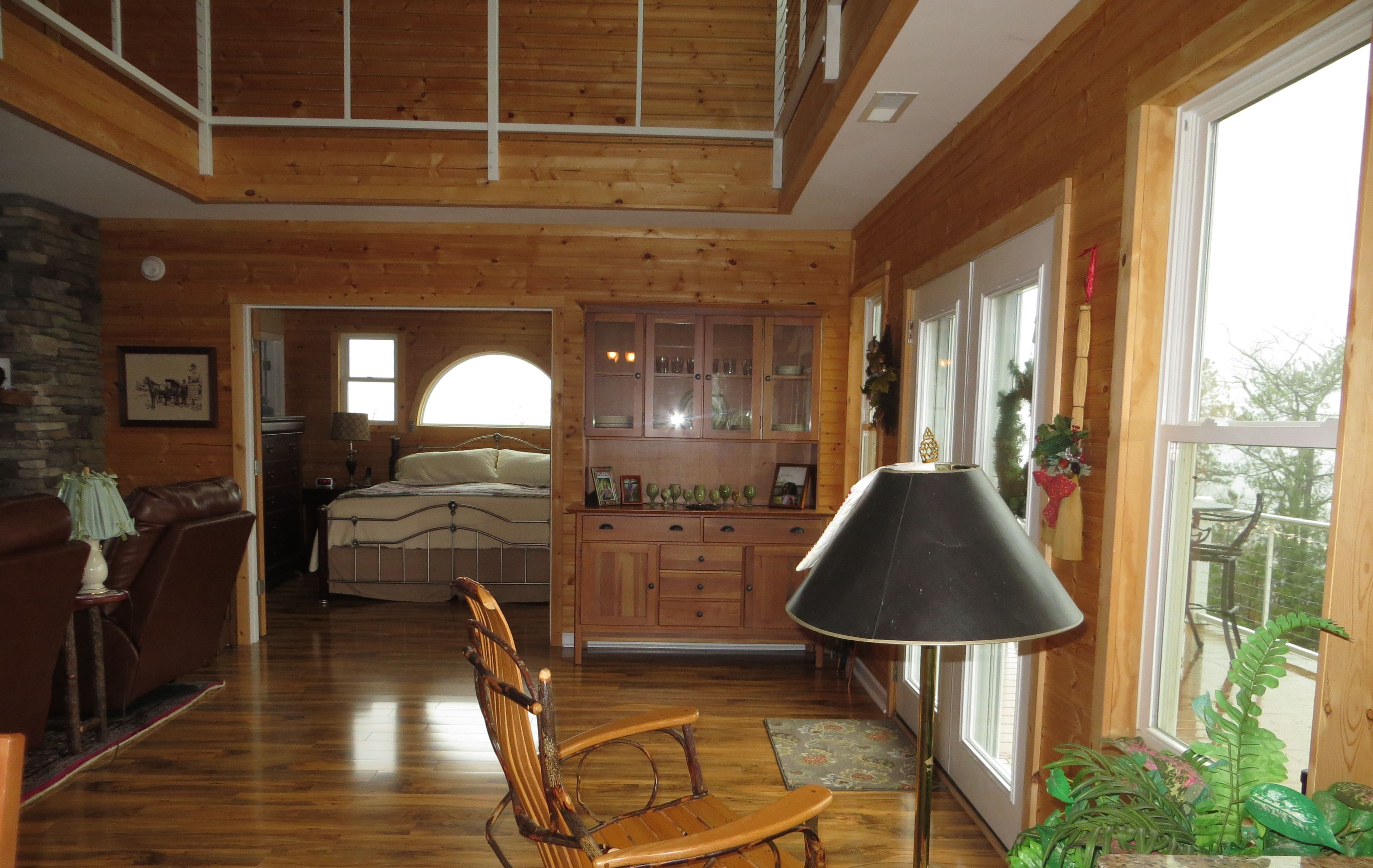 Un salón amplio con techo alto, suelos de madera, un gran ventanal y una zona de estar acogedora.