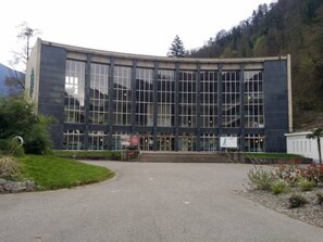 A modern building with large windows, a central entrance, and a paved driveway leading to the entrance.