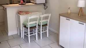 Eine kompakte Küche mit weißen Schränken, einer Mikrowelle, einem kleinen Esstisch mit Stühlen und einem Schrank mit einer Lampe.