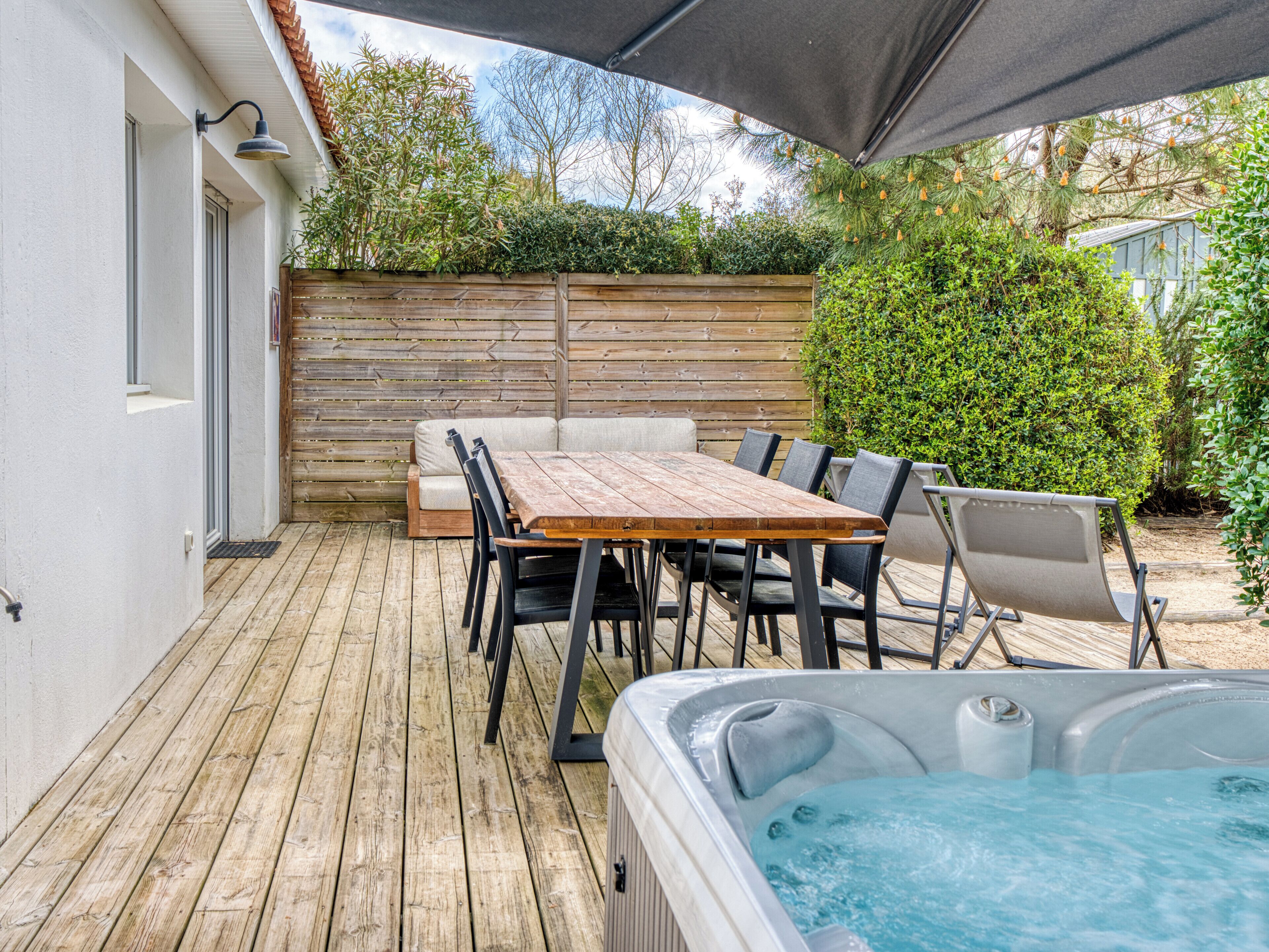 An outdoor patio with a wooden table and chairs, a hot tub, and a wooden fence.