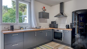 Ett modernt kök med gråa skåp, ett svart kylskåp, en inbyggd ugn och ett fönster med utsikt över grönområden.