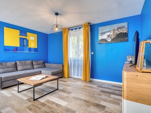 A room with a blue wall, a grey sofa, a wooden coffee table, and a wooden cabinet.