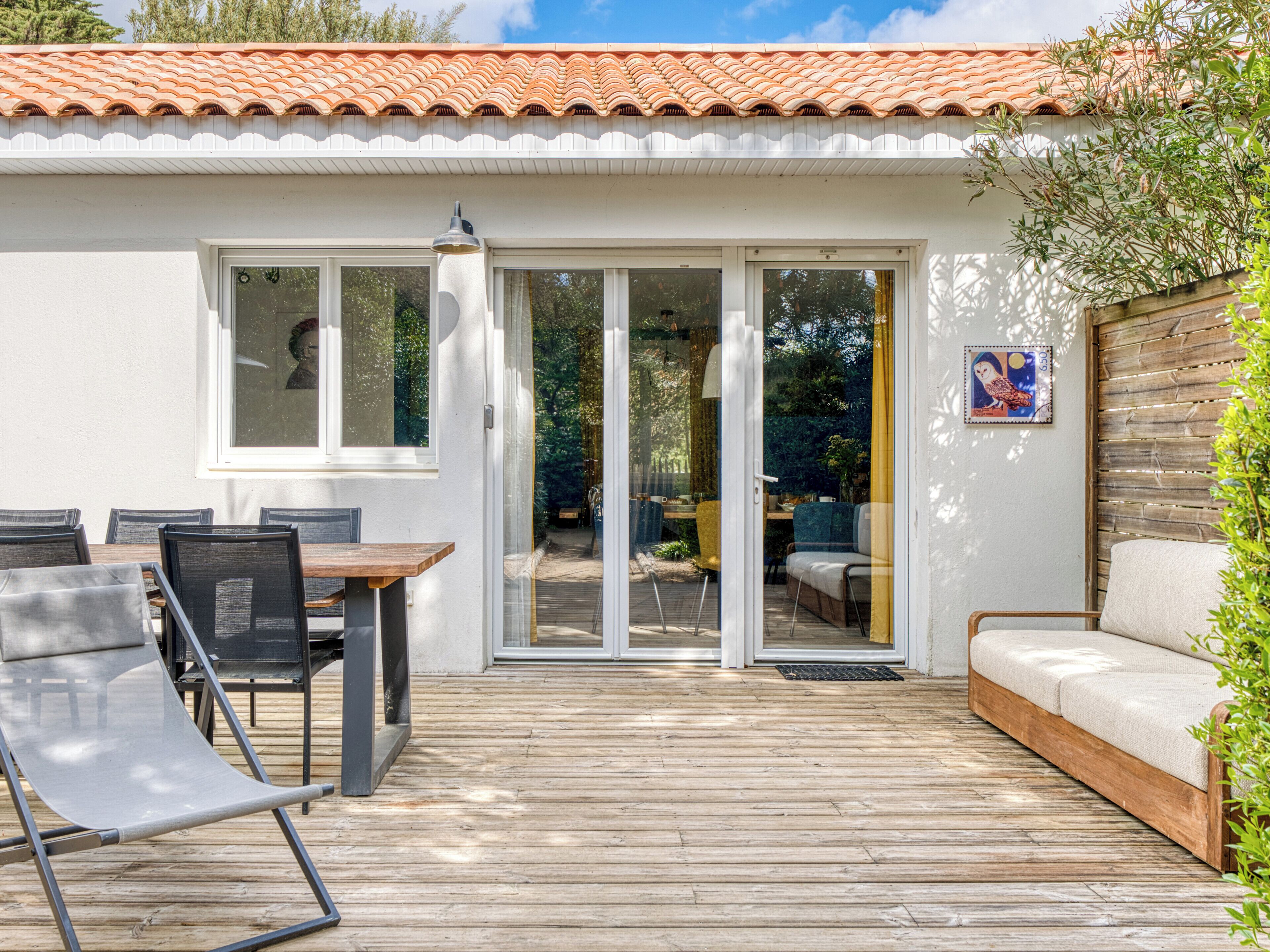 Een huis met een terras, een eethoek met stoelen, een bank en een schuifdeur die uitkomt op een tuin.