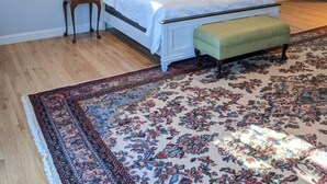 Un dormitorio con techo inclinado, una cama grande con ropa blanca, un banco verde, una alfombra estampada y una lámpara colgante.