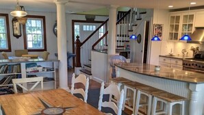 Un comedor amplio con una mesa de madera y sillas blancas, una cocina con electrodomésticos modernos y una escalera que lleva a otro nivel.