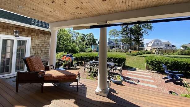 Un patio techado al aire libre con piso de madera, una silla de mimbre y una parrilla.