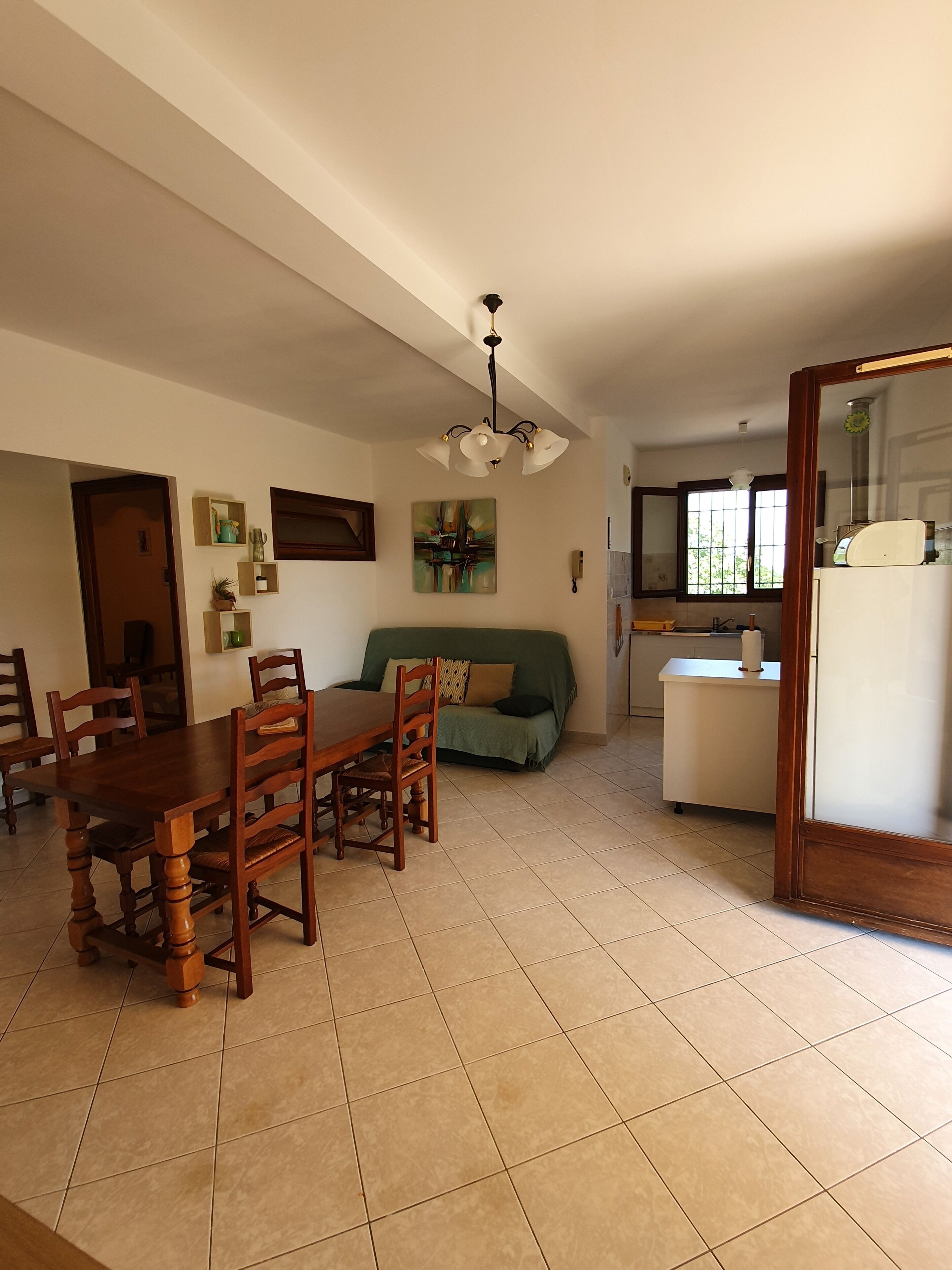 A spacious living area with a dining table, chairs, a sofa, and a kitchen area with a refrigerator.