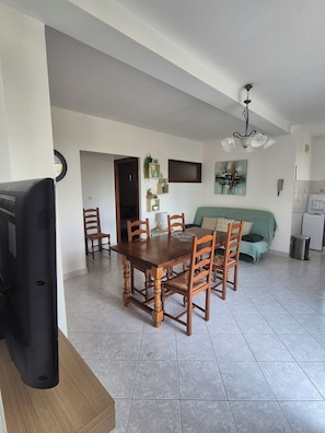 Un coin repas avec une table et des chaises en bois, un téléviseur et, au fond, un canapé vert.