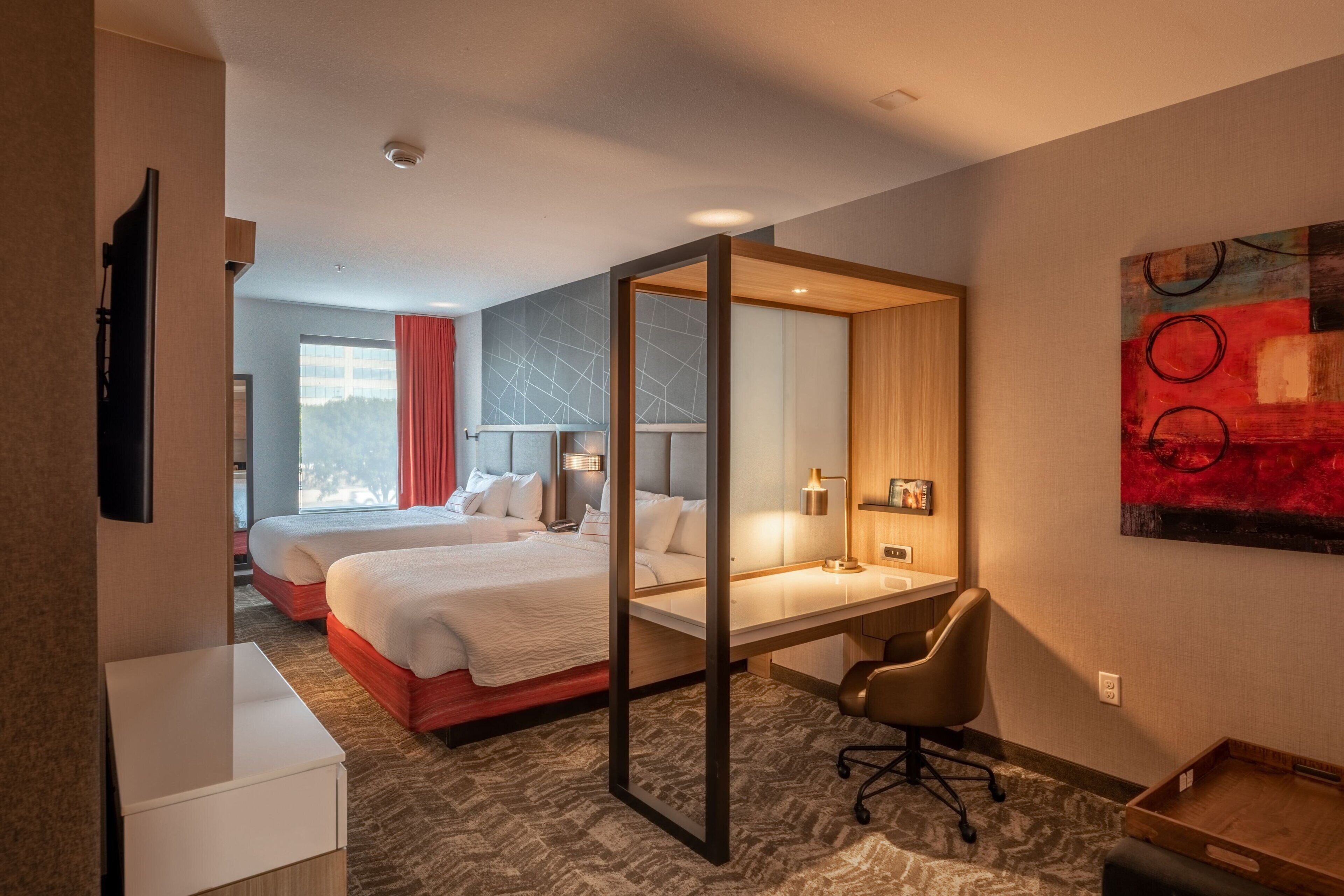Habitación de hotel con dos camas, un escritorio, una silla y un ventanal grande.