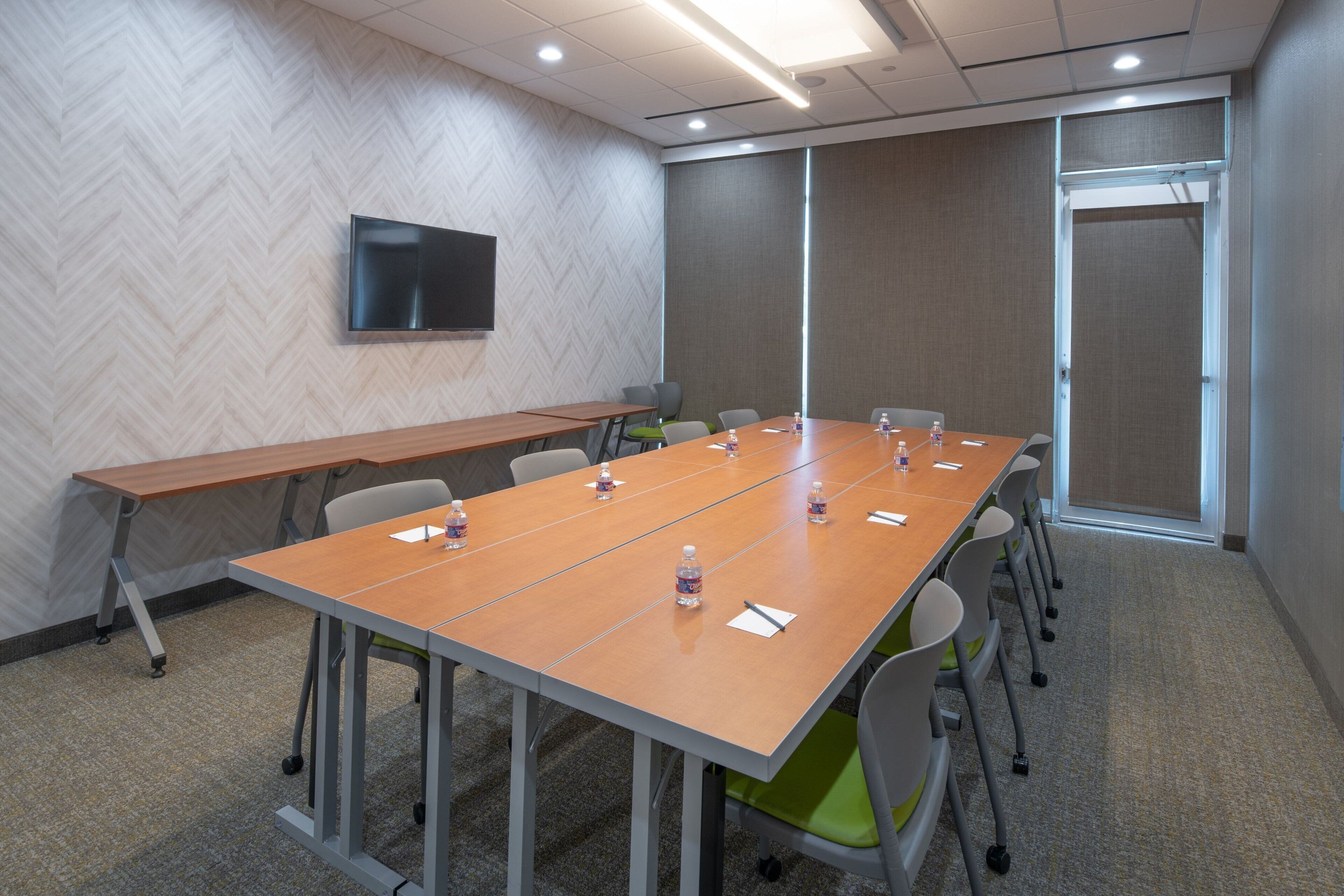 A conference room with a long table, chairs, a flat-screen TV, and a door.