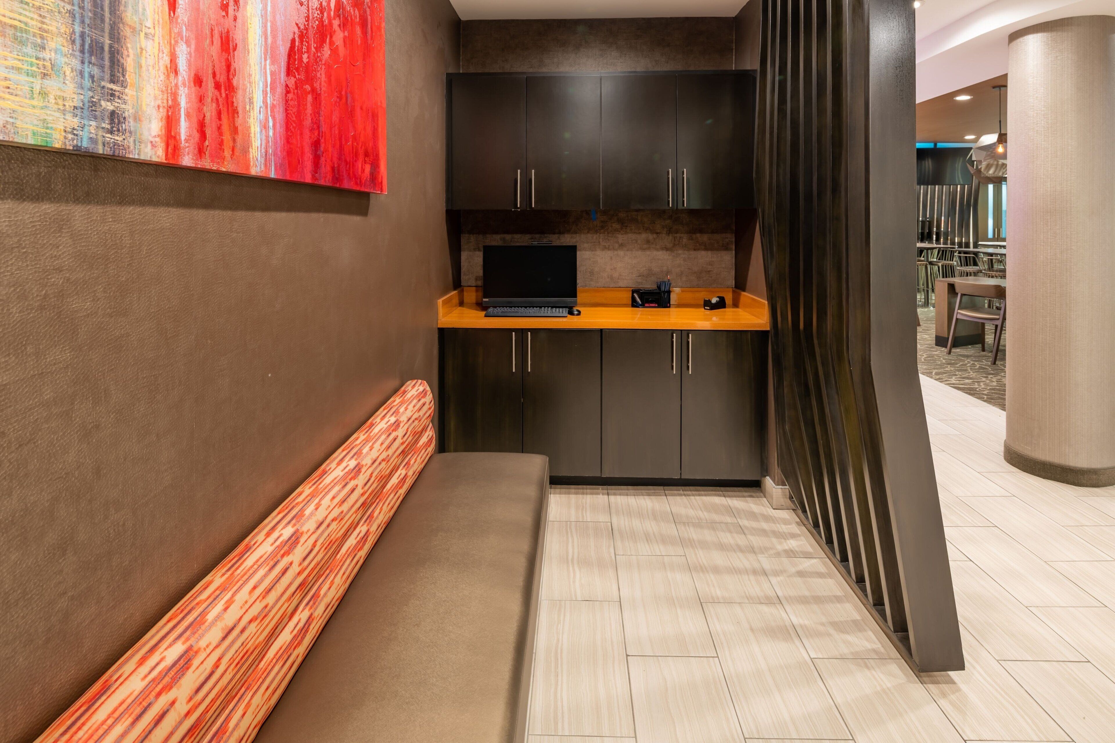 A modern hotel lobby with a seating area, a small kitchenette, and a view into the dining area.