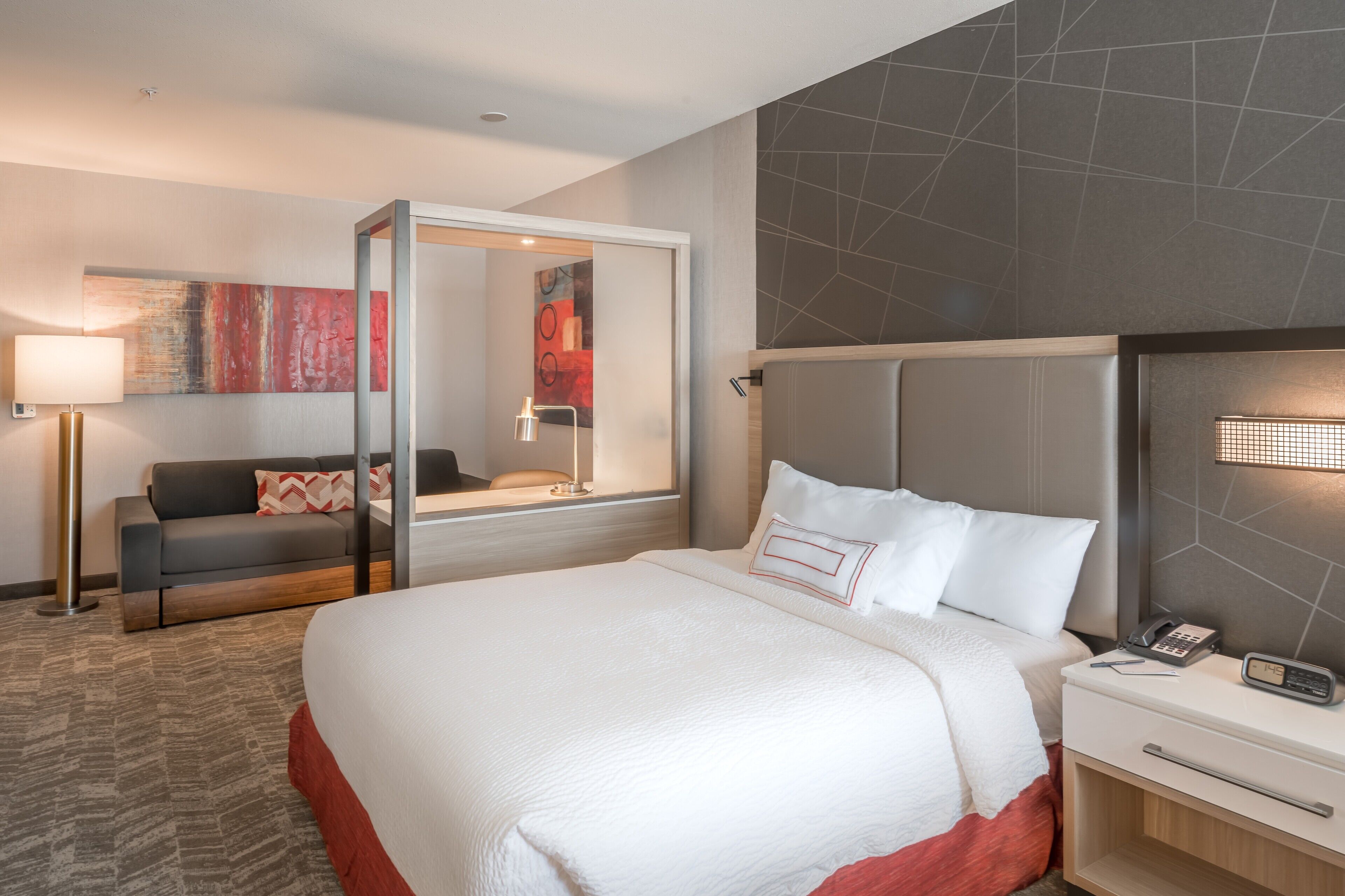 Une chambre d’hôtel moderne avec un grand lit, une table de chevet avec une lampe, un canapé et un grand miroir.