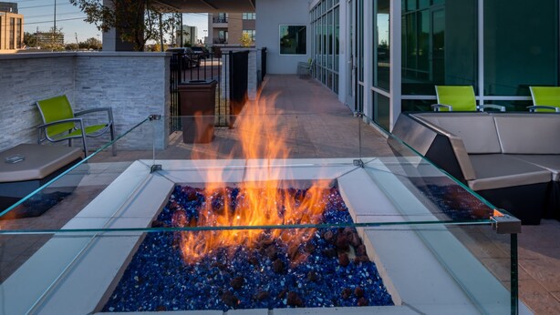 Un espace extérieur moderne, aménagé avec des sièges, un foyer en verre, du mobilier d’extérieur et offrant une vue sur la façade du bâtiment.