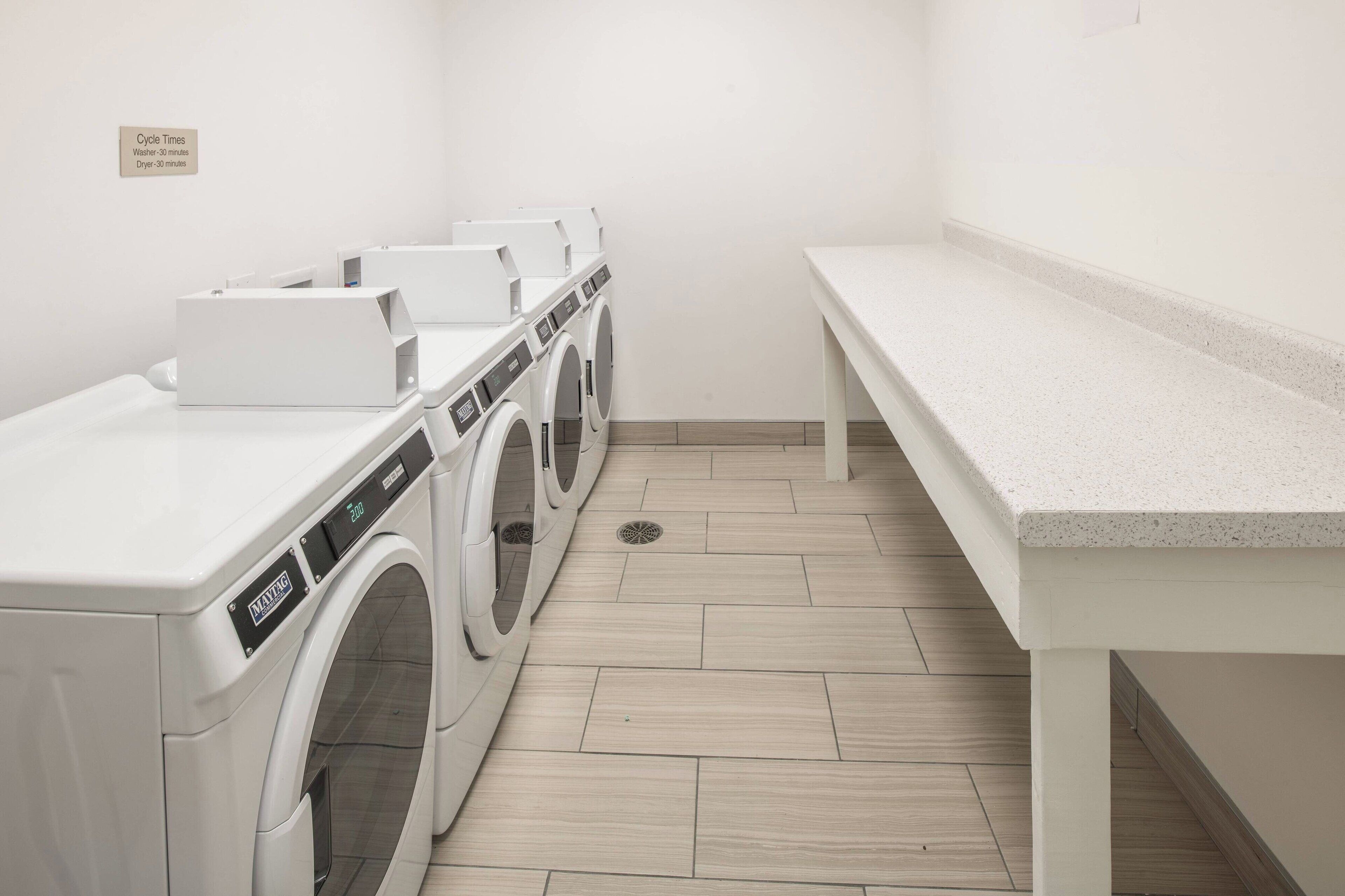 A laundry room with three white washing machines and a bench.