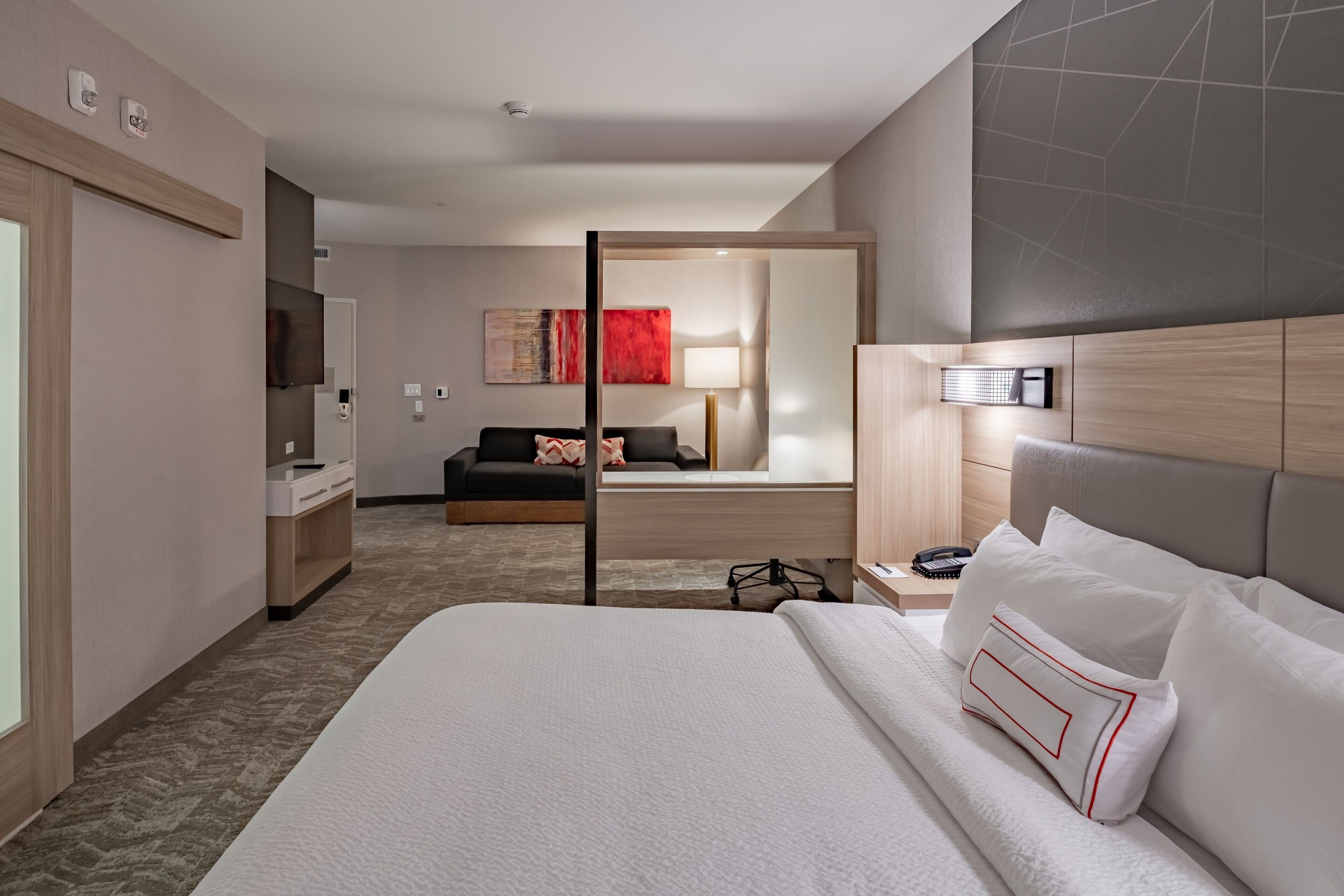 Une chambre d’hôtel moderne dotée d’un grand lit, d’un bureau, d’une télévision et d’un coin salon séparé avec un canapé et une lampe.