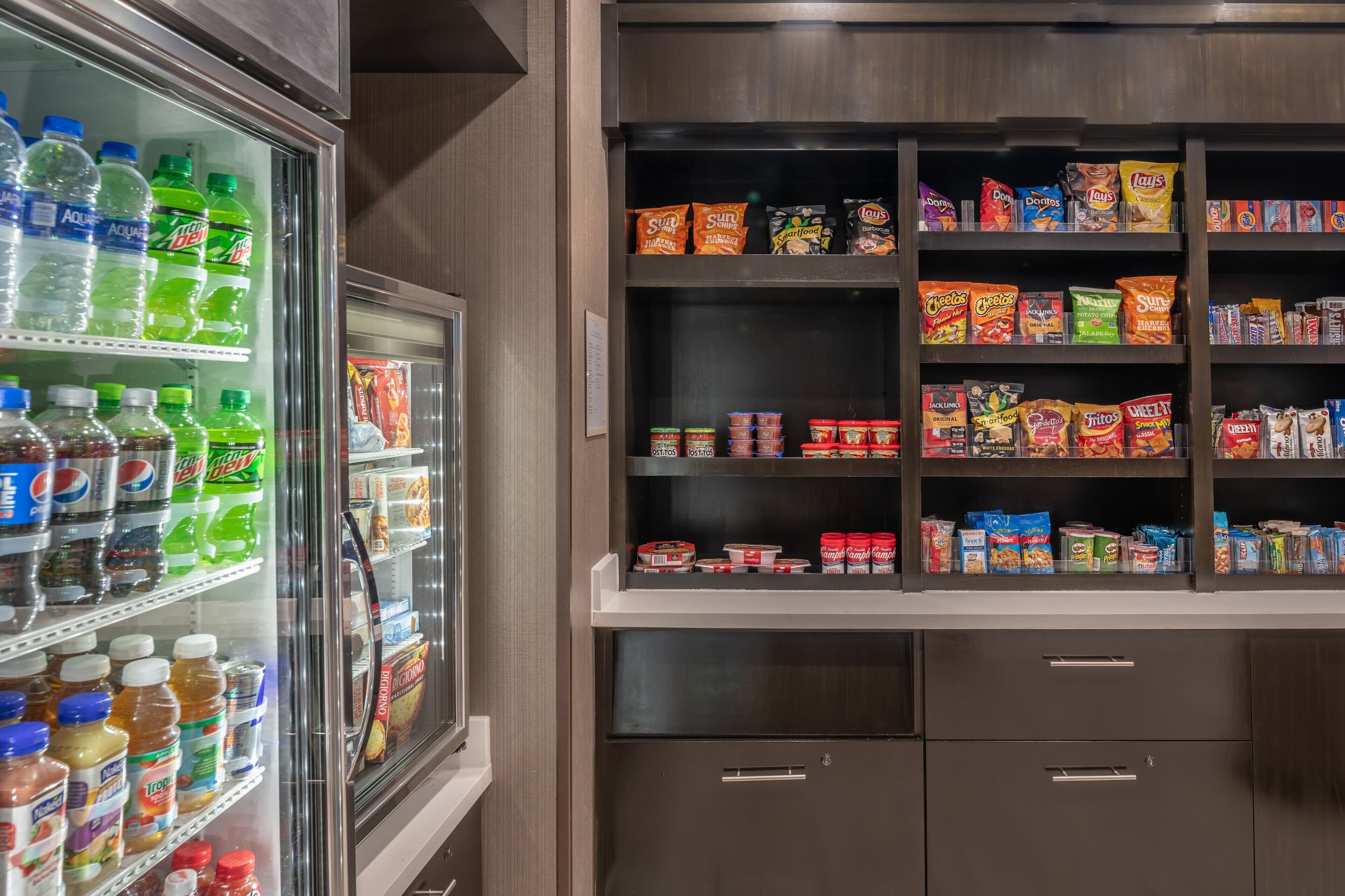 A refrigerated beverage cooler stocked with various drinks and a pantry shelf with snacks and cereals.