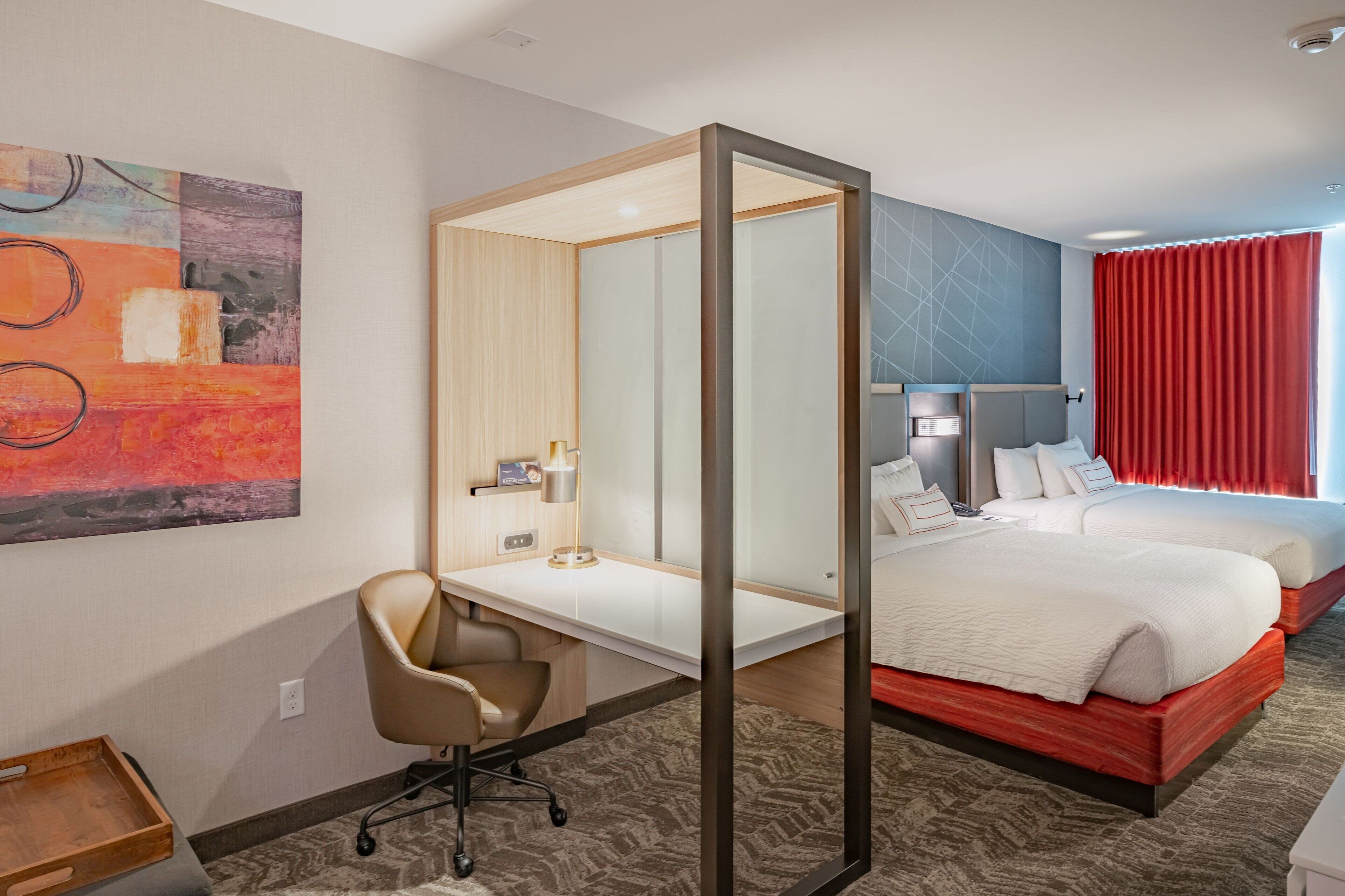 Habitación de hotel con escritorio, cama, silla y un espejo grande.