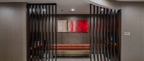 Un área de recepción moderna con un banco, un cuadro abstracto grande y un cartel que dice 'Business Center'.