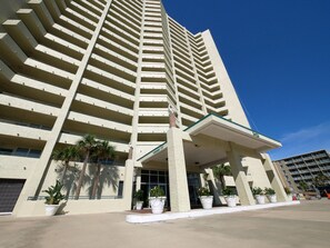 Un edificio alto con un design architettonico moderno, caratterizzato da un ingresso ben visibile con una tettoia e diverse piante in vaso.