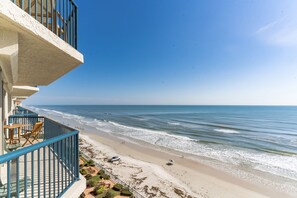 Un balcone affacciato sulla spiaggia, con vista sull'oceano, sulla sabbia e su un cielo sereno.