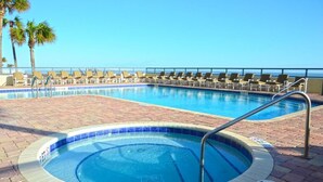 Une piscine dotée de chaises longues et d’un jacuzzi, entourée d’une terrasse en briques et de palmiers.