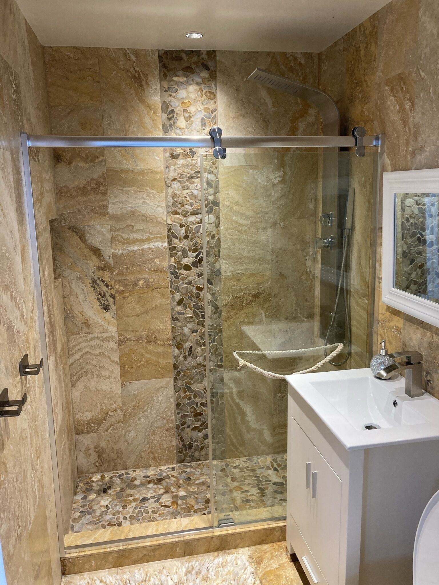 Un baño con ducha de vidrio, lavamanos con espejo y pared de piedra.