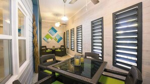 A dining area with a glass table, wicker chairs, and a ceiling fan. - Boat House Beach Suite by Island House Vacation Rentals (West Bay)