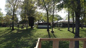 A grassy outdoor area with trees and a building in the background. - Spacious Norfork Lake View Bunkhouse, Resort Amenities, Family/Fishermen/Pets (Gamaliel)