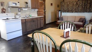 A kitchen with a stove, microwave, and wooden cabinets. There is a dining table with chairs and a sofa in the living area. - Spacious Norfork Lake View Bunkhouse, Resort Amenities, Family/Fishermen/Pets (Gamaliel)
