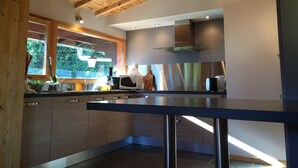 A modern kitchen with wooden beams, a large window, and stainless steel appliances. - 90m² chalet overlooking Lake Annecy (Saint-Jorioz)