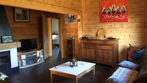 A cozy living room with a fireplace, wooden walls, a television, and a painting. - 90m² chalet overlooking Lake Annecy (Saint-Jorioz)