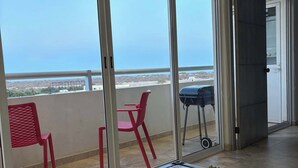 Un balcon avec vue sur la mer, une chaise rouge, une chaise bleue et une table avec une plante.