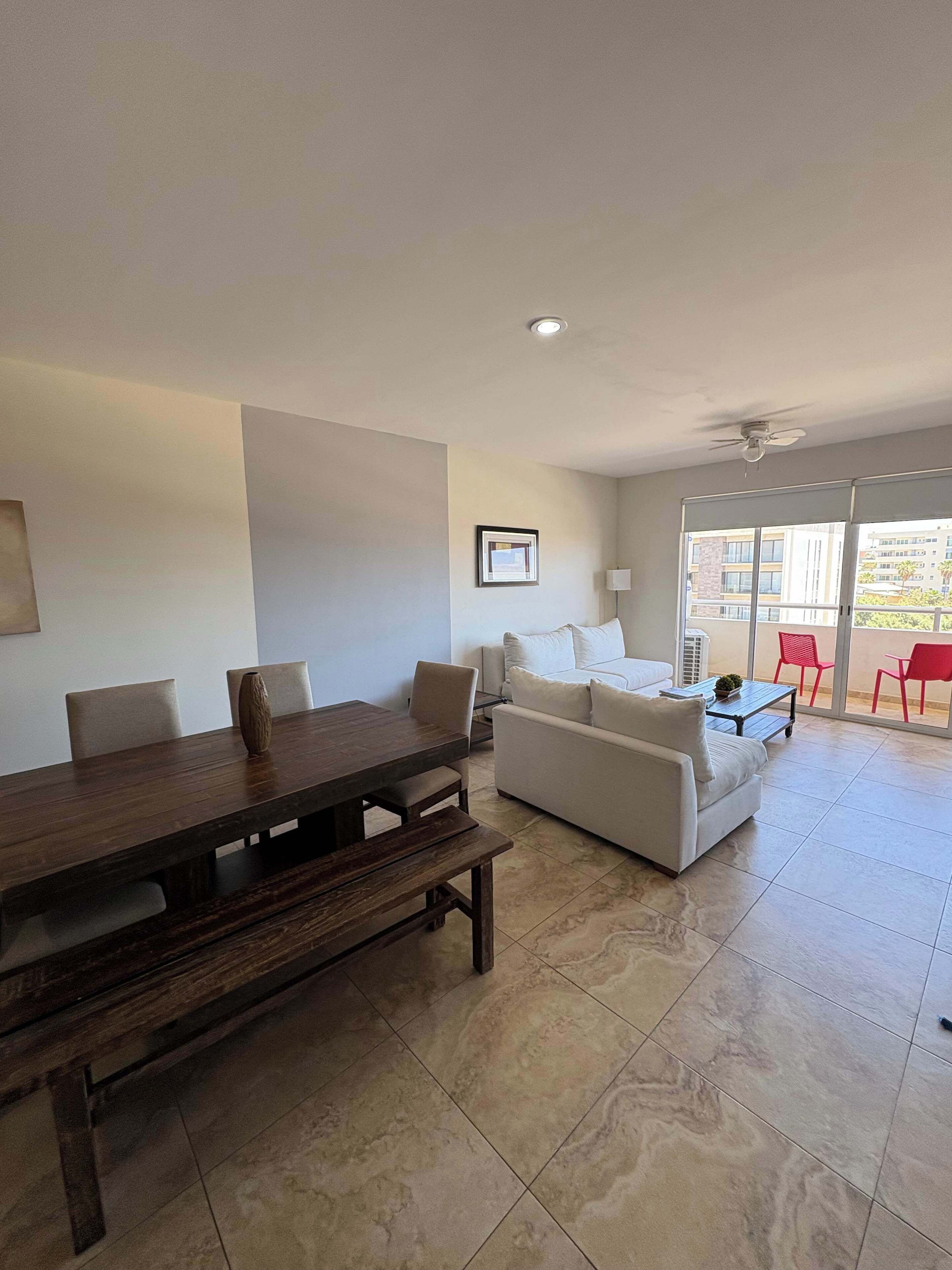 A spacious living area with a wooden dining table, a sofa, and a balcony with red chairs.