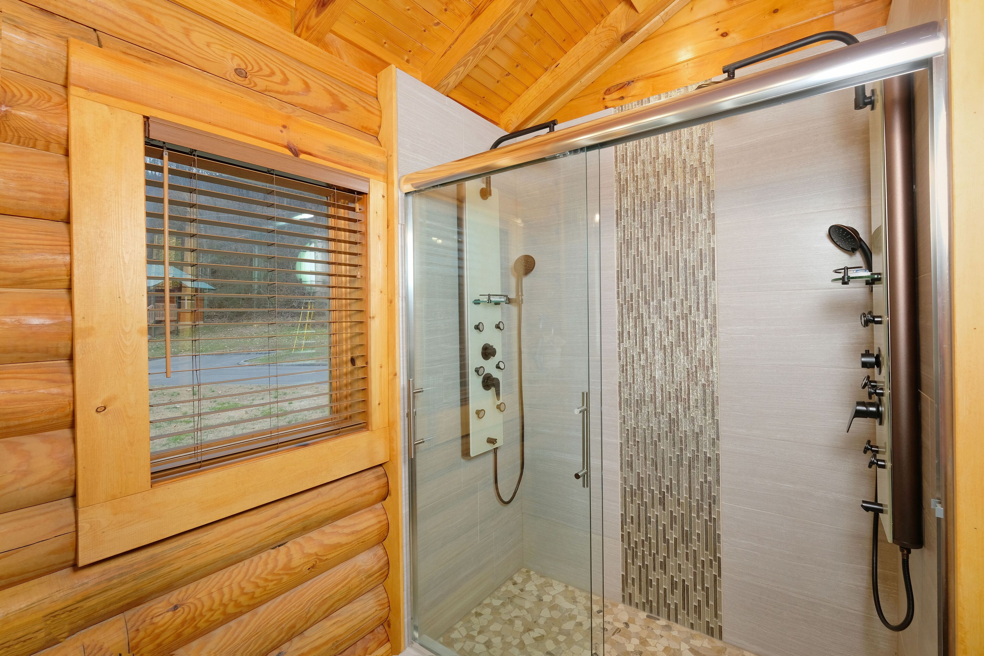 A wooden cabin with a glass-enclosed shower area, wooden walls, and a window with blinds.