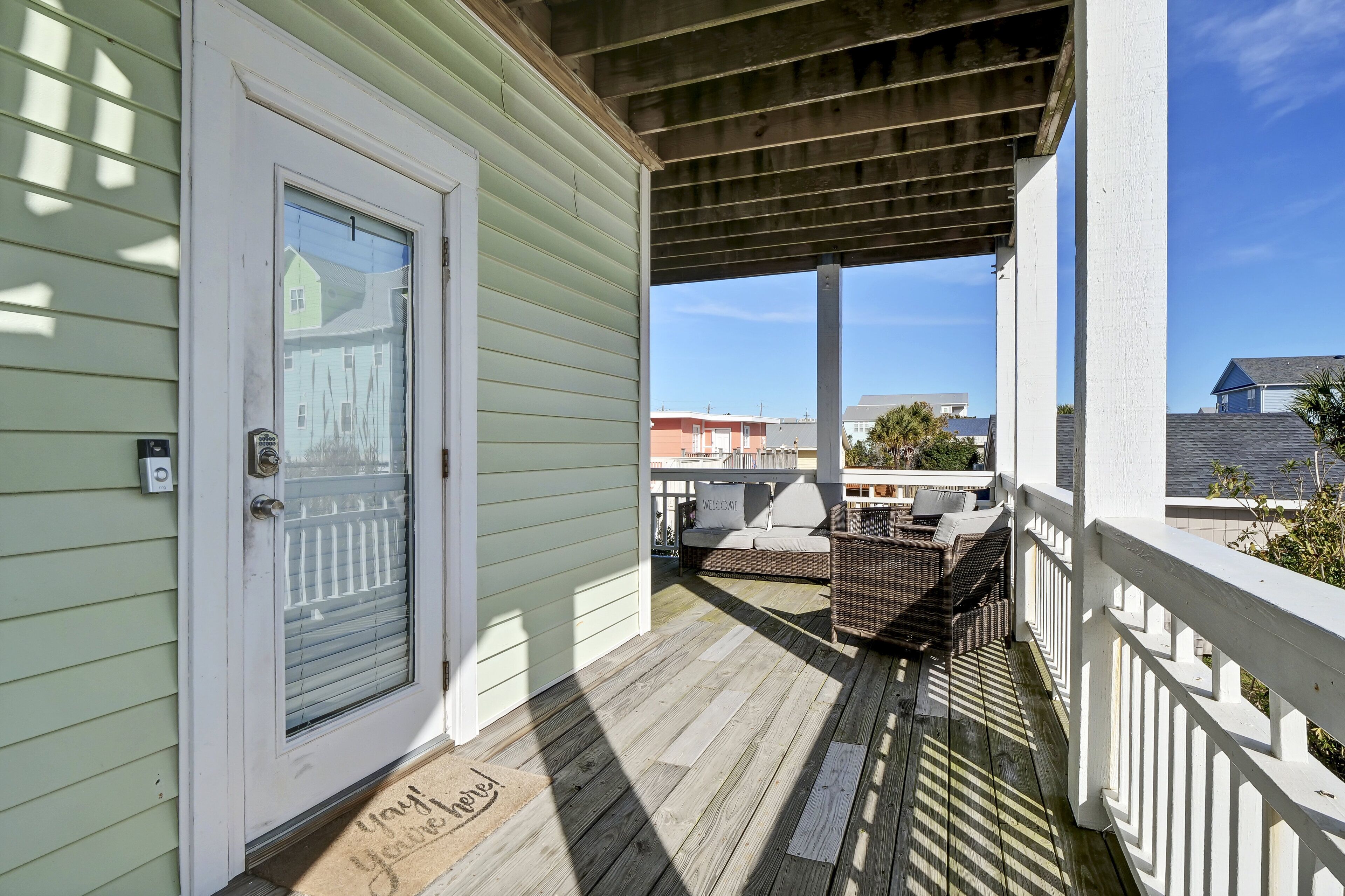 A wooden deck with a white railing, a door with a glass panel, and a welcome mat.